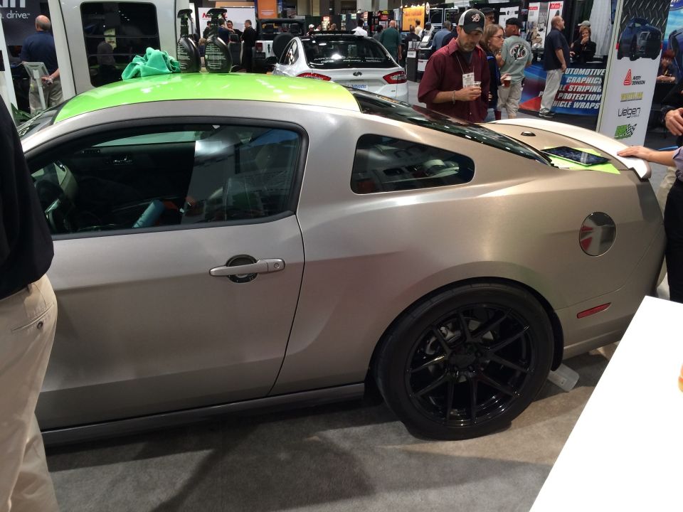 Silver Ford Mustang coupe with green roof wrap and black wheels at an auto show.