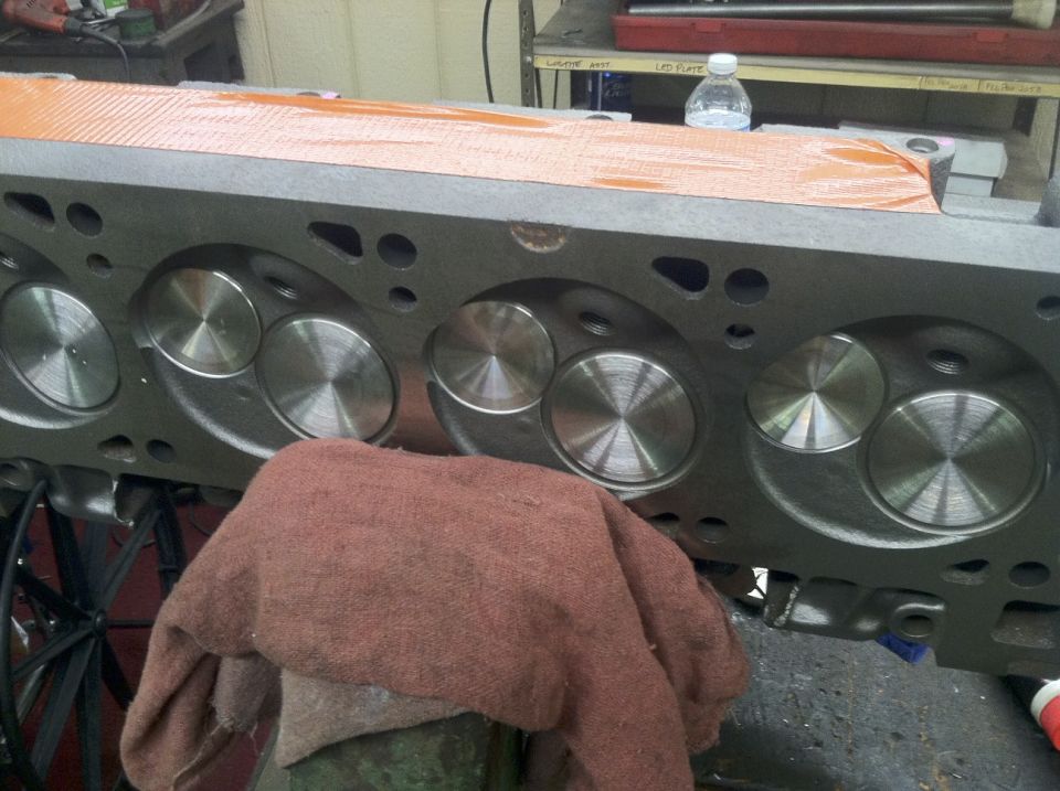 Gray V8 engine cylinder head with polished valves and an orange protective sheet.