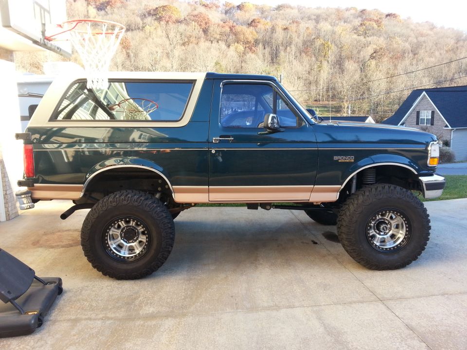 Lifted 1995 Ford Bronco, dark green with tan top, parked on concrete driveway.