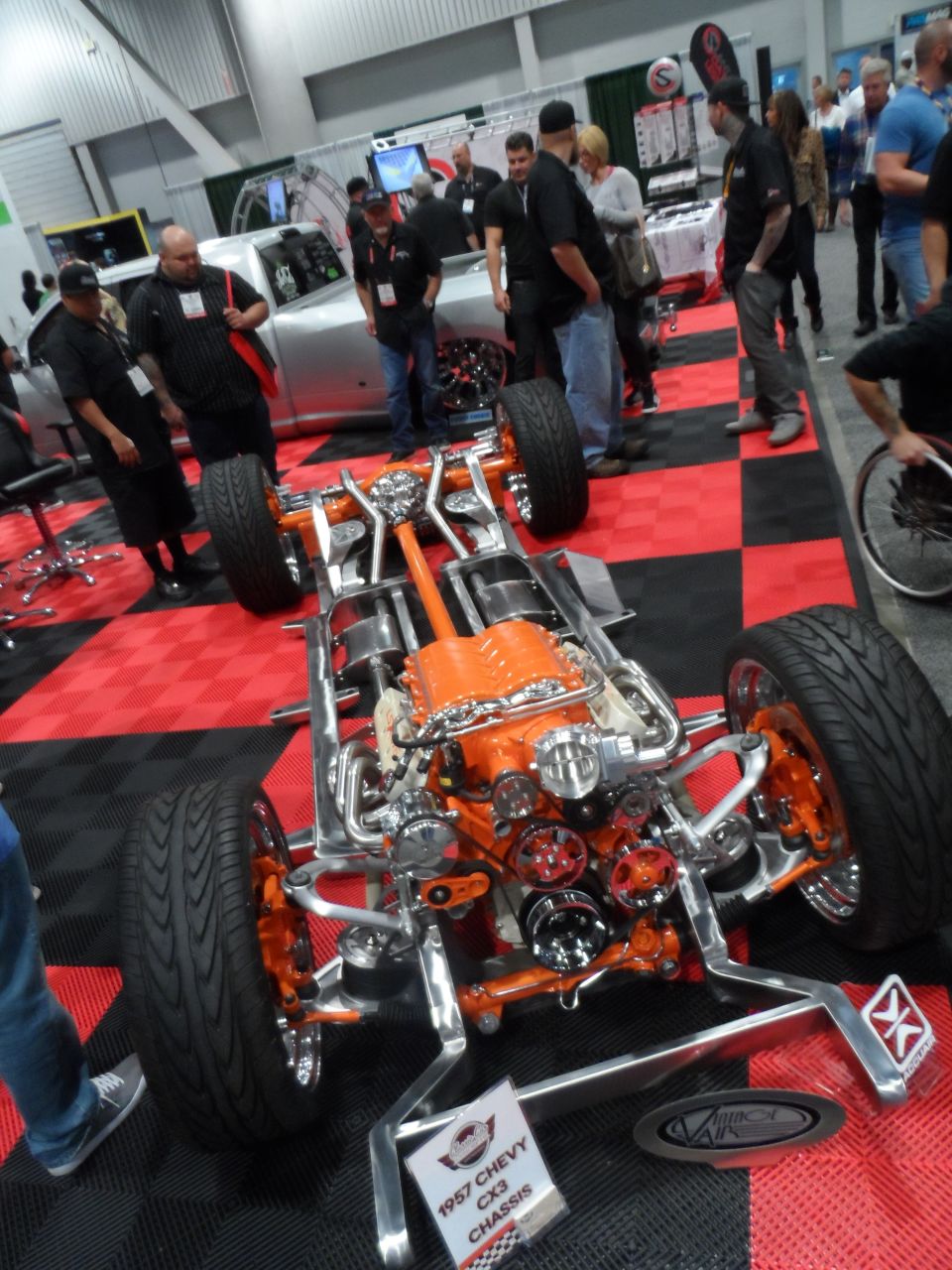 1957 Chevy CX3 chassis with orange engine and polished metal frame on display.