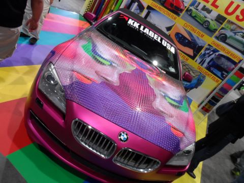 1971 Ford Ranchero - A pink BMW 6 Series coupe with a custom graphic wrap featuring a stylized face is displayed at an automotive show. The car is parked on a c…