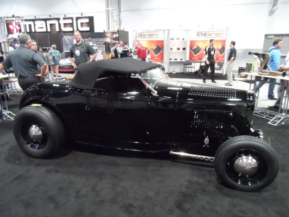 Black convertible hot rod with chrome accents on display at an indoor event.