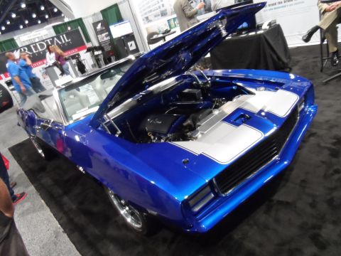 1971 Ford Ranchero - A bright blue custom convertible with the hood open, revealing the engine, is displayed on a black carpeted floor at an indoor event. The c…