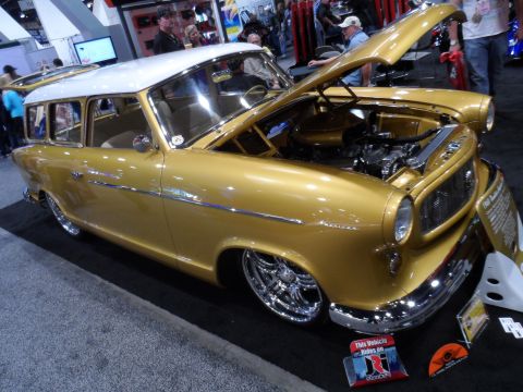 1971 Ford Ranchero - A gold AMC Rambler American station wagon with a white roof is displayed with its hood open, revealing the engine. The car is lowered with…