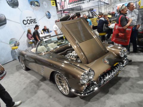 1971 Ford Ranchero - A custom brown convertible with its hood open, revealing the engine, is displayed indoors at an auto show. The car features chrome accents…