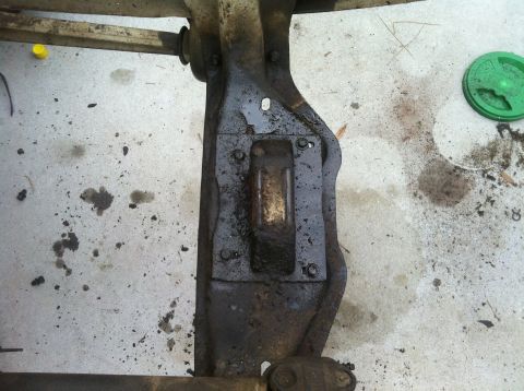 1979 Ford Bronco - A close-up view of a vehicle's undercarriage part, showing mechanical components and oil stains on the ground.