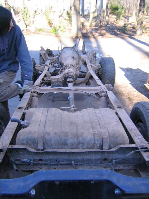 1978 Ford Bronco - The chassis and drivetrain of a vehicle are shown, with a person observing.