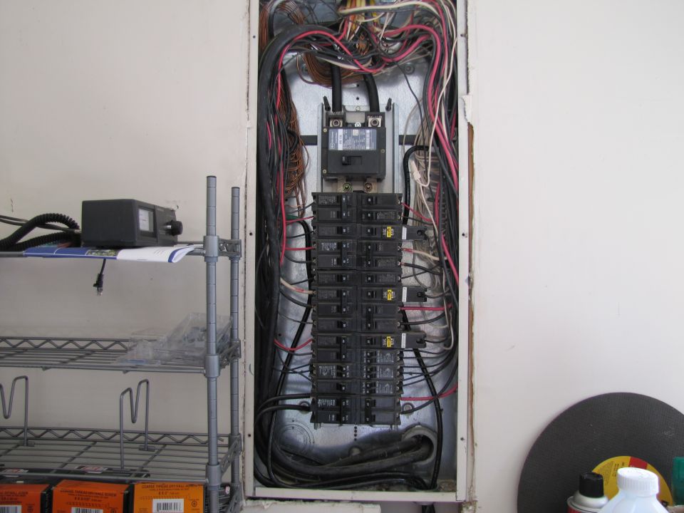 Electrical panel with circuit breakers and wiring, next to a metal shelf.