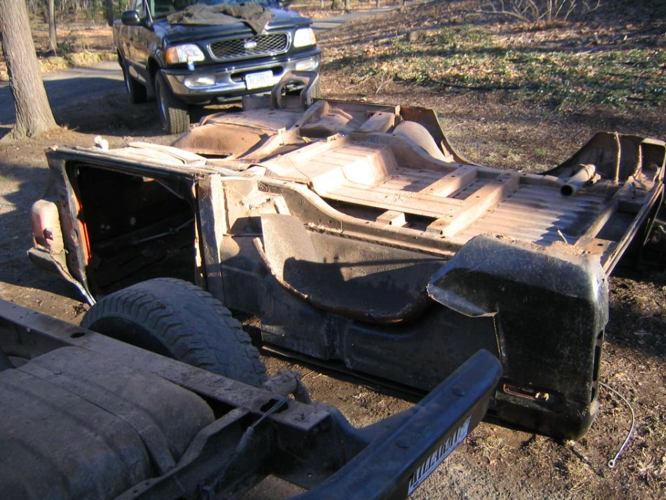 Rusted vehicle chassis with a pickup truck in the background
