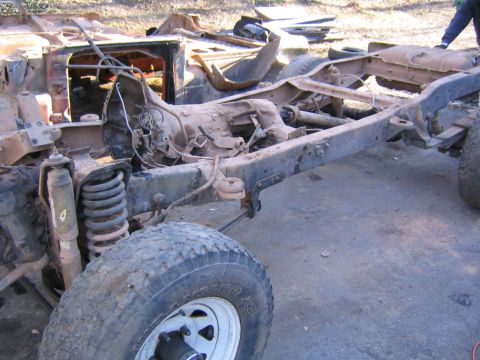 1978 Ford Bronco - The chassis of a 1978 Ford Bronco, showing its frame, transmission, and suspension components, lies in a scrapyard.
