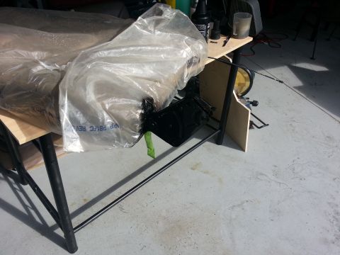 1994 Ford Bronco - A black mechanical part, covered in plastic, sits on a workbench next to various tools and containers.