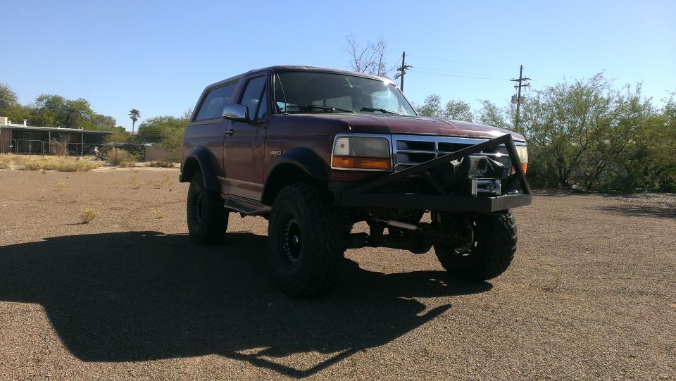 Maroon Ford Bronco with aftermarket bumper and winch, lifted suspension, off-road tires, parked on gravel lot