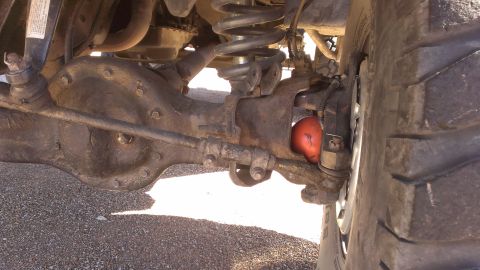 1996 Ford Bronco - The front axle and suspension of a vehicle are shown in detail, with a bright orange shock absorber visible near the wheel.