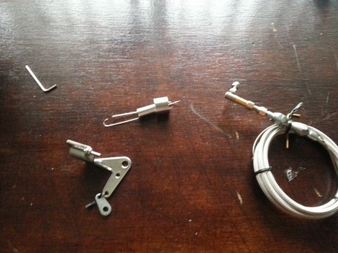 1981 Ford Bronco - Various carburetor linkage components and a braided cable are laid out on a wooden surface.