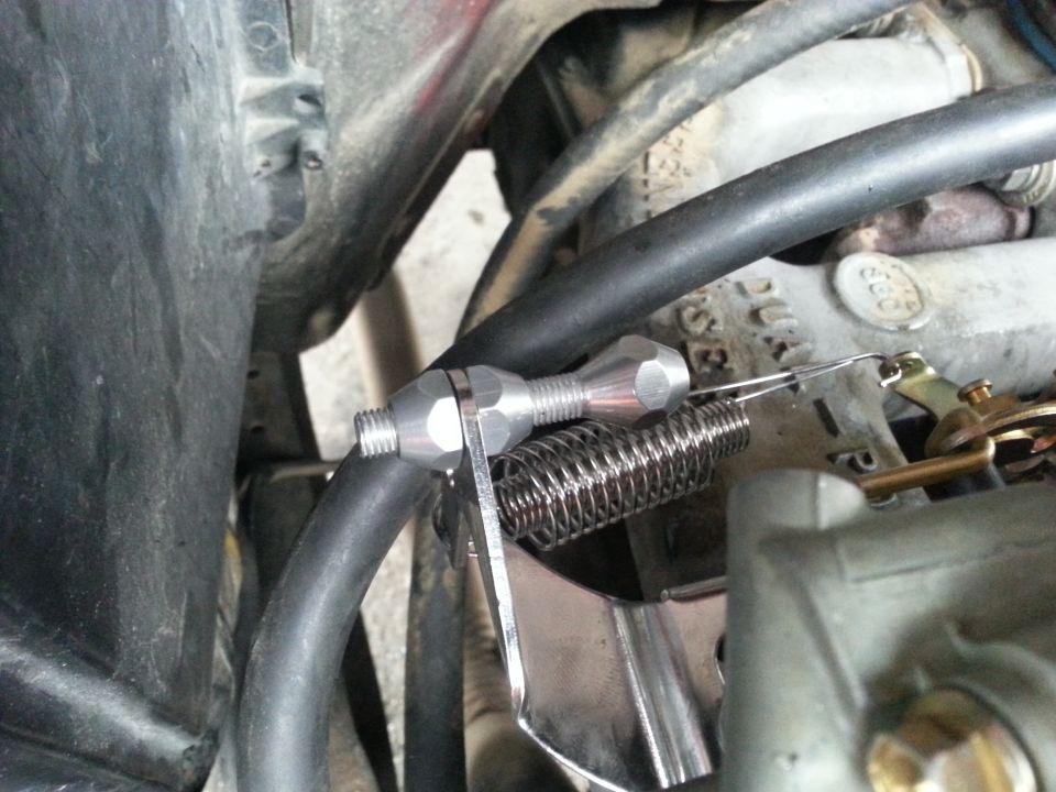 Close-up of a silver throttle cable linkage with a spring attached to a carburetor