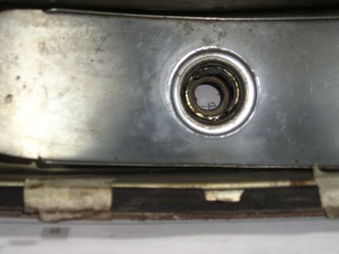 1975 Ford Courier - A close-up view of a metal bracket with a central opening, revealing internal details and some text below.
