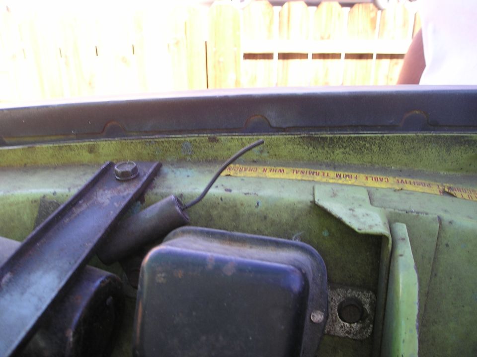 Close-up of a green engine bay with a black electrical component and a yellow warning label