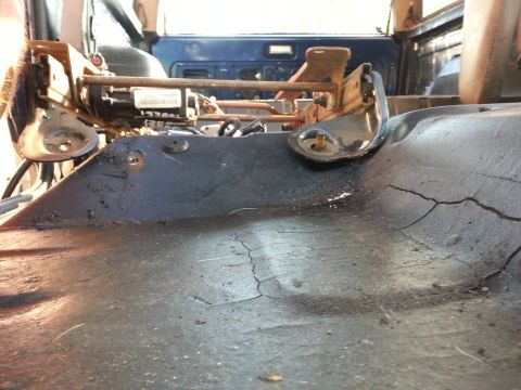 1994 Ford Bronco - Close-up of the seat mounting hardware and a cracked floor panel inside a vehicle.