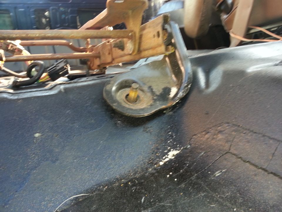 Close-up of a rusty metal seat mounting bracket attached to a black surface