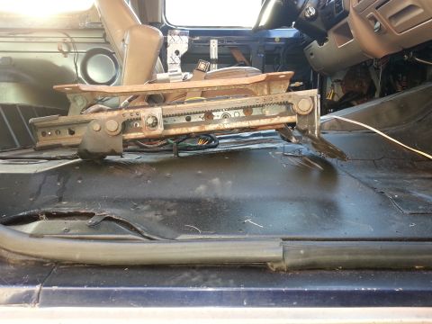 1994 Ford Bronco - The interior of a blue vehicle shows exposed floor and seat rails after the driver's seat has been removed.