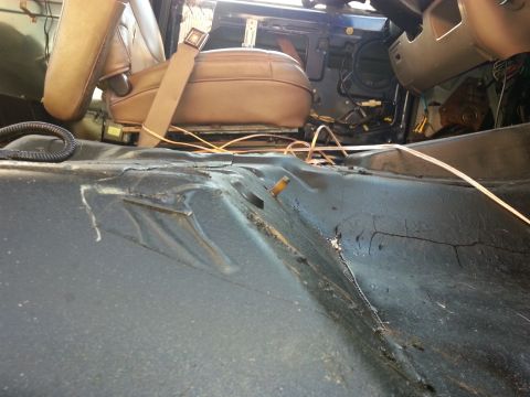 1994 Ford Bronco - The interior floor of a vehicle shows significant wear and tear on the matting, with a tan seat and seatbelt visible.