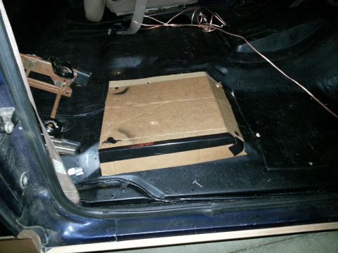 1994 Ford Bronco - The interior floor of a blue vehicle shows a section covered by cardboard, with copper wiring running across the dark carpet.