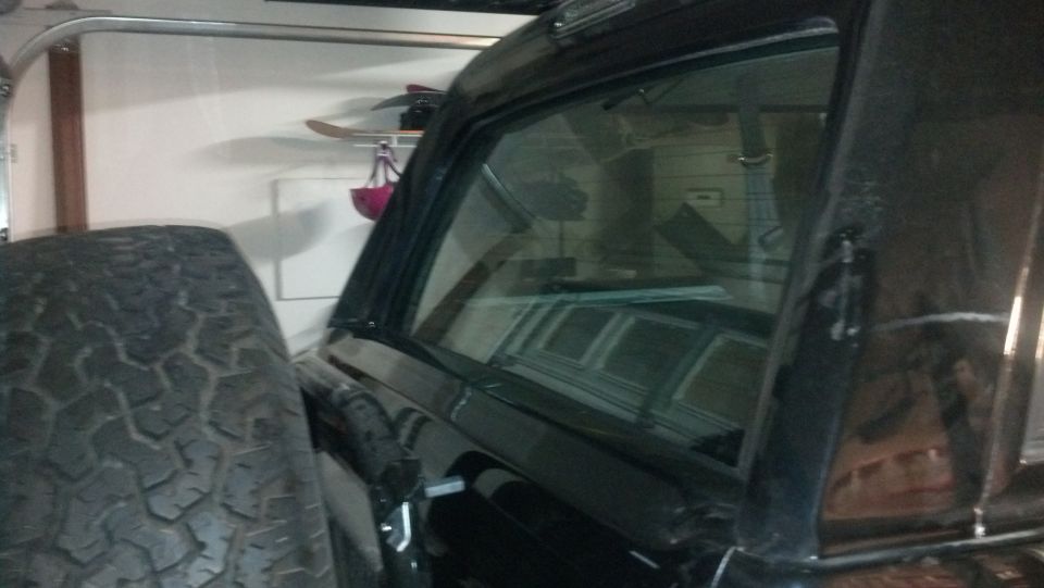 Black SUV side view, spare tire visible, interior reflection shows horizontal lines