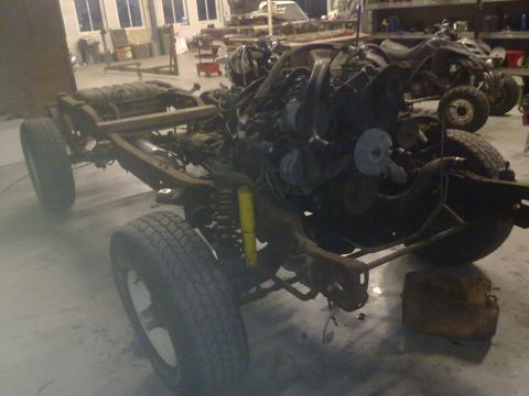 1984 Ford Bronco - The frame and engine of a vehicle are shown in a garage, with other vehicles in the background.