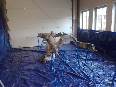1984 Ford Bronco - A vehicle frame is being worked on inside a garage, with blue tarps covering the floor and walls.