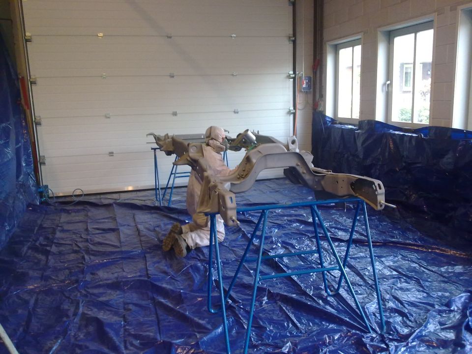 Vehicle frame on sawhorses, covered in blue tarp, inside a garage