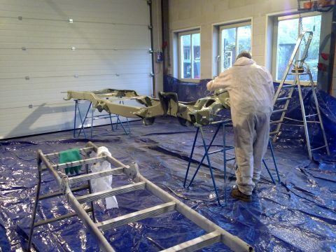 1984 Ford Bronco - A vehicle frame is being painted in a garage setting.