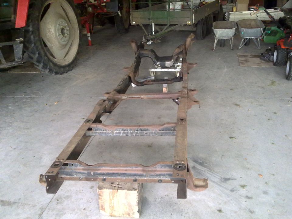 Vehicle frame on blocks, with tractor and trailer in background