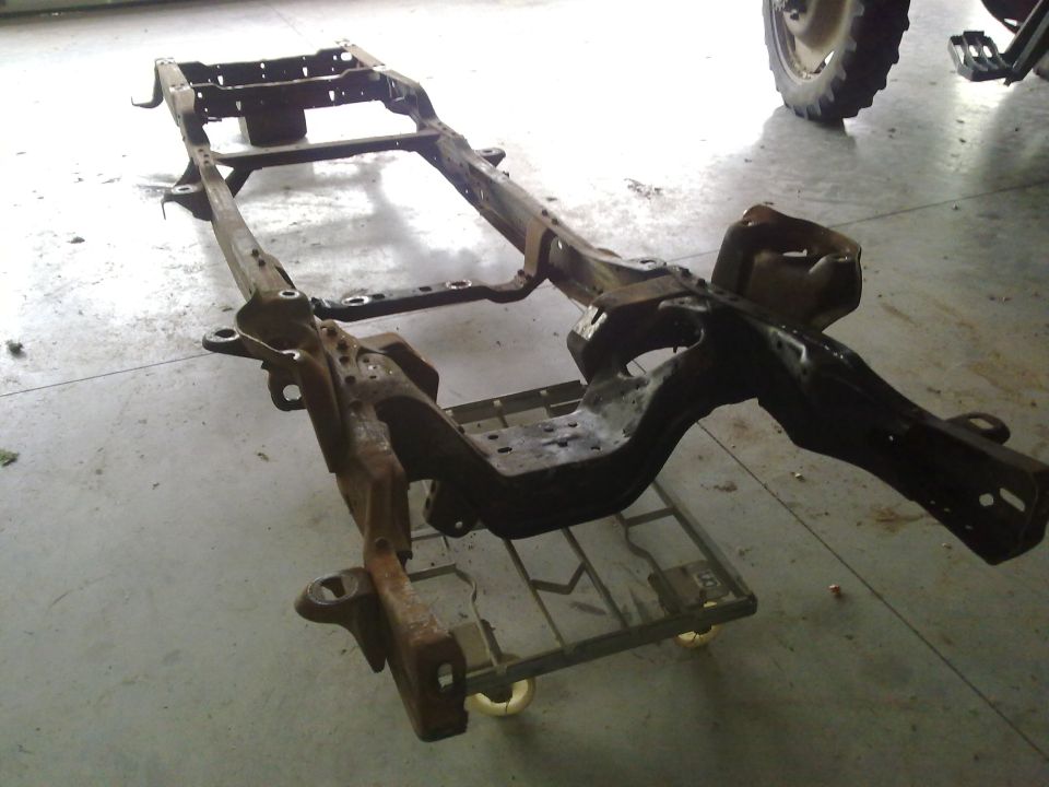 Vehicle frame assembly on a rolling dolly, with a tire visible in the background