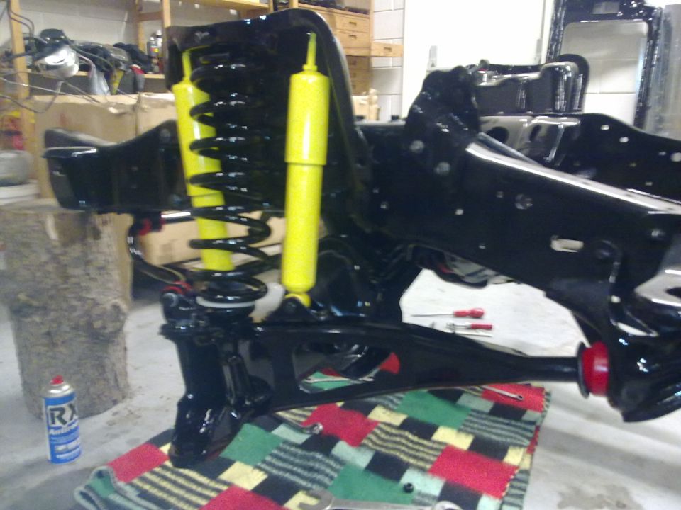 Black painted front suspension assembly with yellow shocks and black springs. A can of spray lubricant is on the left