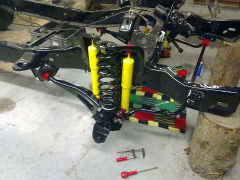 1984 Ford Bronco - The chassis and suspension of a vehicle are visible, supported by logs and tools on the floor.