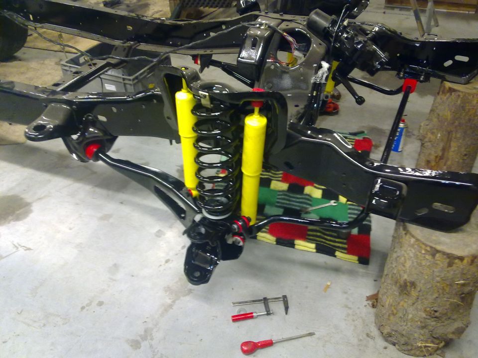 Vehicle chassis with yellow shock absorbers and black springs, undergoing repair