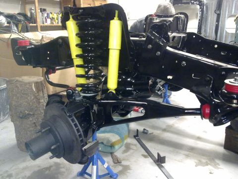 1984 Ford Bronco - Close-up of a vehicle's suspension and chassis during a rebuild, showing new black components and bright yellow shock absorbers.