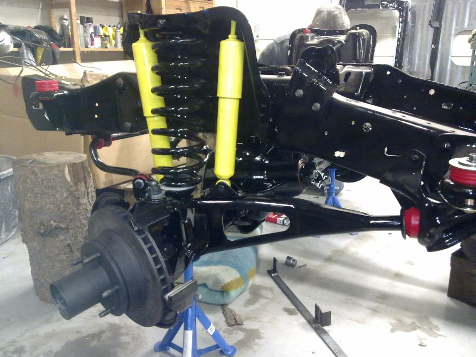 Black chassis with yellow shocks and black springs on jack stands, front wheel hub visible