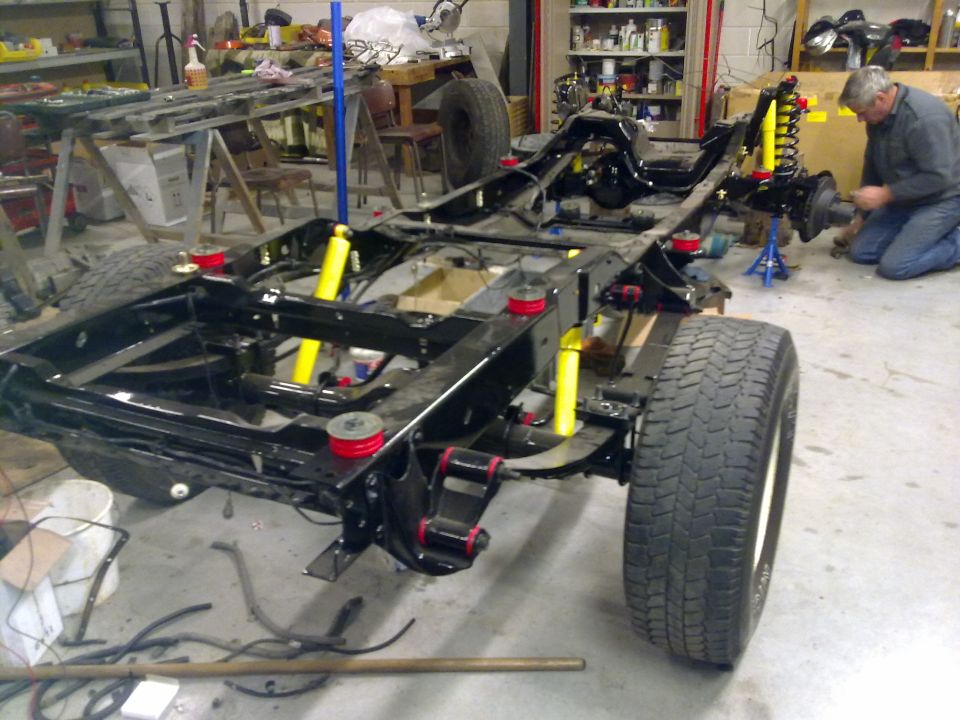 Vehicle chassis with yellow shocks and red suspension bushings. A man works on the rear axle