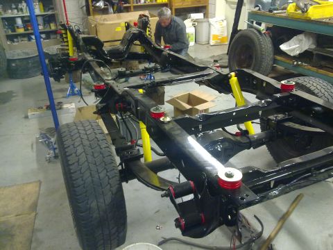 1984 Ford Bronco - A vehicle's frame is shown with new suspension components installed, with a person working in the background.