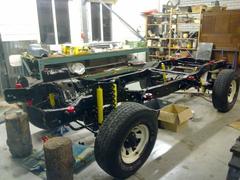 1984 Ford Bronco - The chassis of a 1984 Ford Bronco is shown during a rebuild, with suspension components and wheels clearly visible.