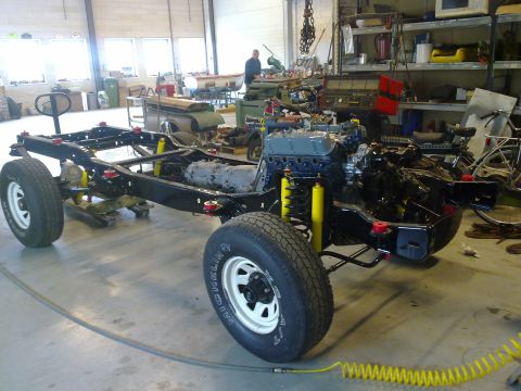 1984 Ford Bronco - The frame and powertrain of a vehicle are assembled in a garage setting.
