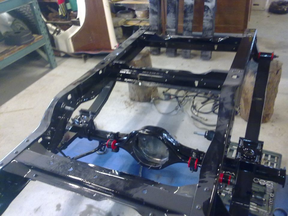 Vehicle frame and rear axle assembly, possibly undergoing restoration. Red bushings are visible on the axle
