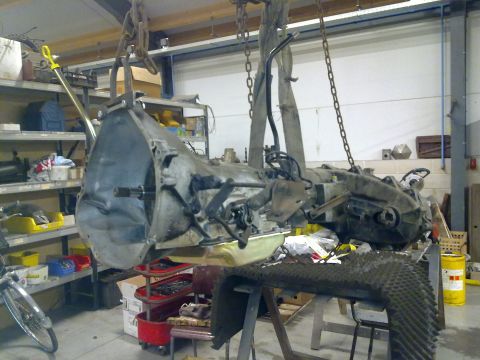 1984 Ford Bronco - Transmission and transfer case assembly suspended by chains in a workshop setting.