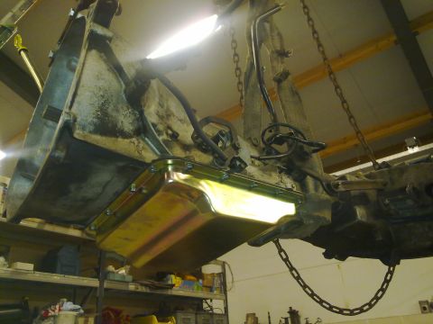 1984 Ford Bronco - Engine oil pan and transmission assembly being worked on, suspended by chains in a workshop.