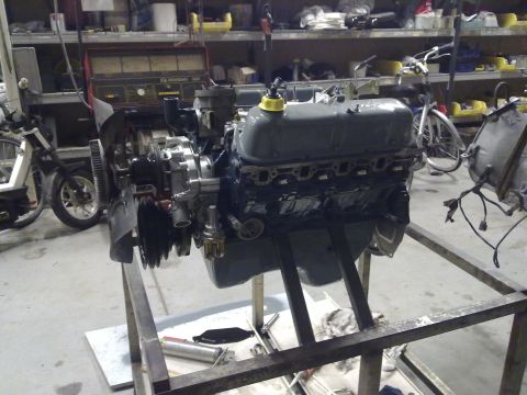 1984 Ford Bronco - Engine assembly on a stand in a workshop setting, with shelves and equipment in the background.