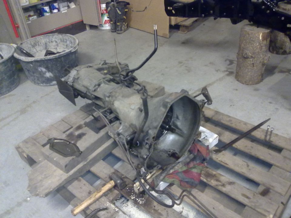 Transmission assembly on wooden pallets, with tools and buckets nearby
