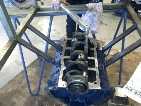 1984 Ford Bronco - Engine block and crankshaft assembly under repair, with a person using a torque wrench.