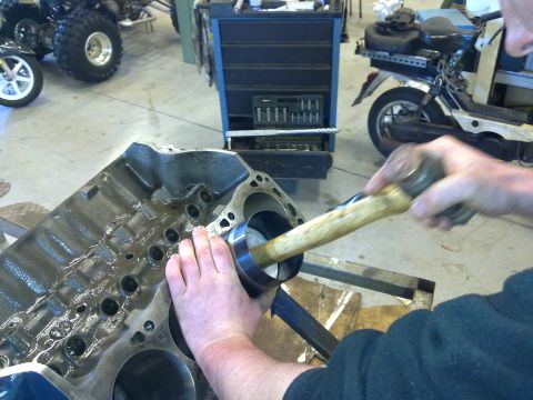1984 Ford Bronco - Mechanic installs a piston into an engine block, with a scooter and ATV visible in the background.
