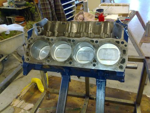1984 Ford Bronco - This is a close-up view of an engine block with pistons installed, resting on a stand in a workshop.